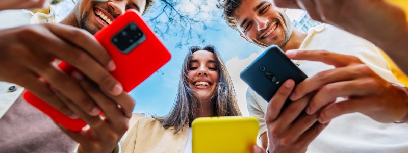 Group of friends smiling while looking at their smartphones outdoors