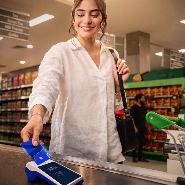 Woman taps a Visa card on a payment terminal at a grocery store checkout